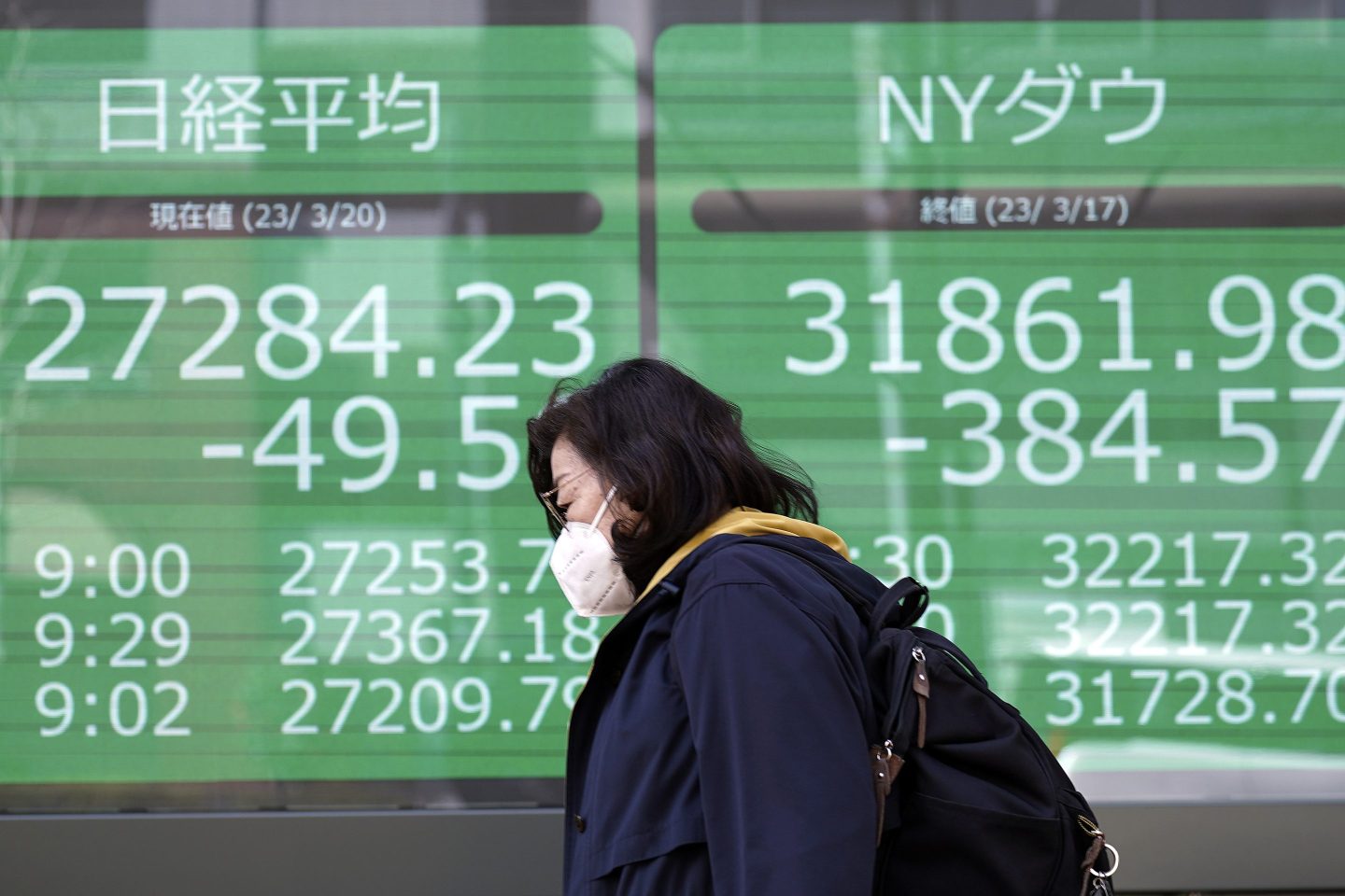 A person walks in front of an electronic stock board showing Japan's Nikkei 225 and New York Dow indexes at a securities firm on March 20, 2023, in Tokyo.