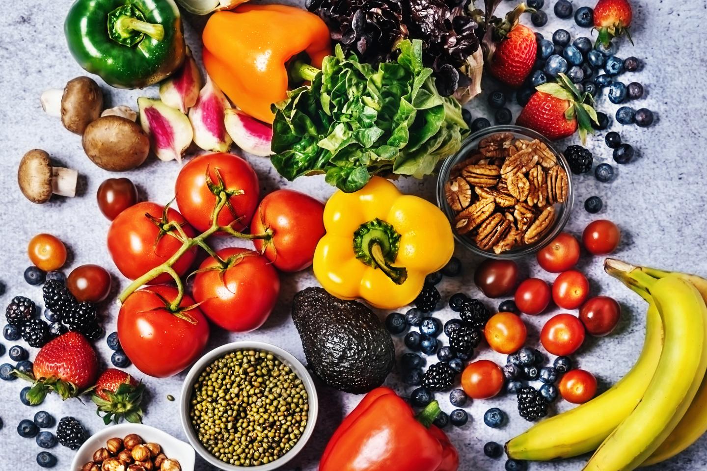 Fresh vegetables, fruits, beans, and nuts on gray background.