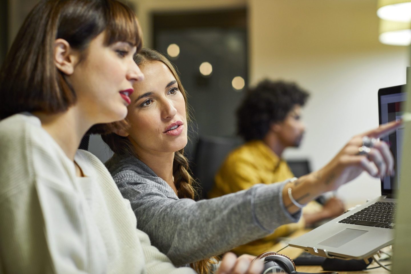 Two women look at a computer monitor, while one points at the screen.