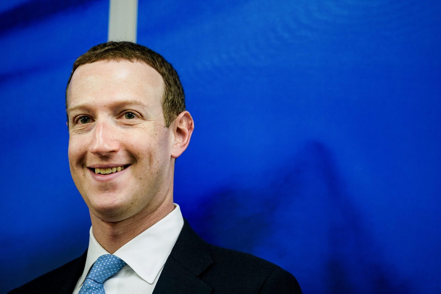 Mark Zuckerberg stands smiling against a blue background