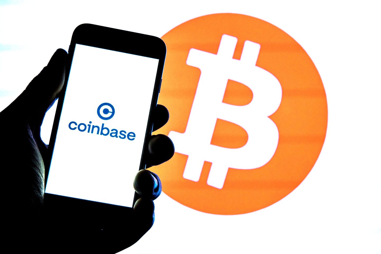 Coinbase logo seen displayed on a smartphone with a Bitcoin logo in the background
