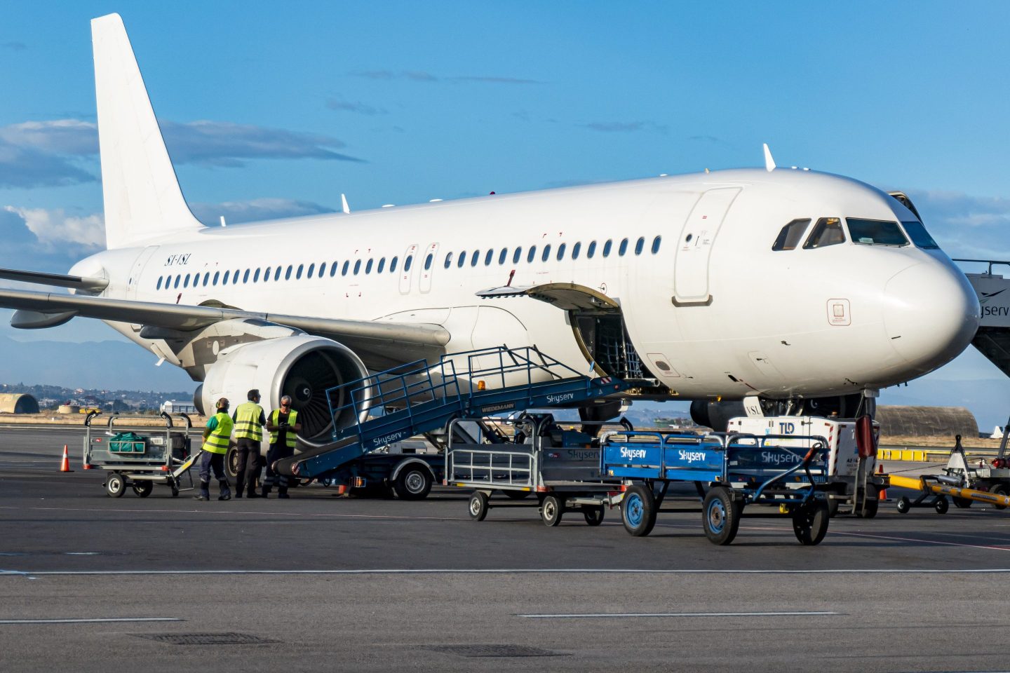 A white passenger plane on the apron without any logo or identification. An Airbus A320 jet aircraft as seen getting loaded with luggage in its belly cargo compartment in Thessaloniki Airport Makedonia SKG. 