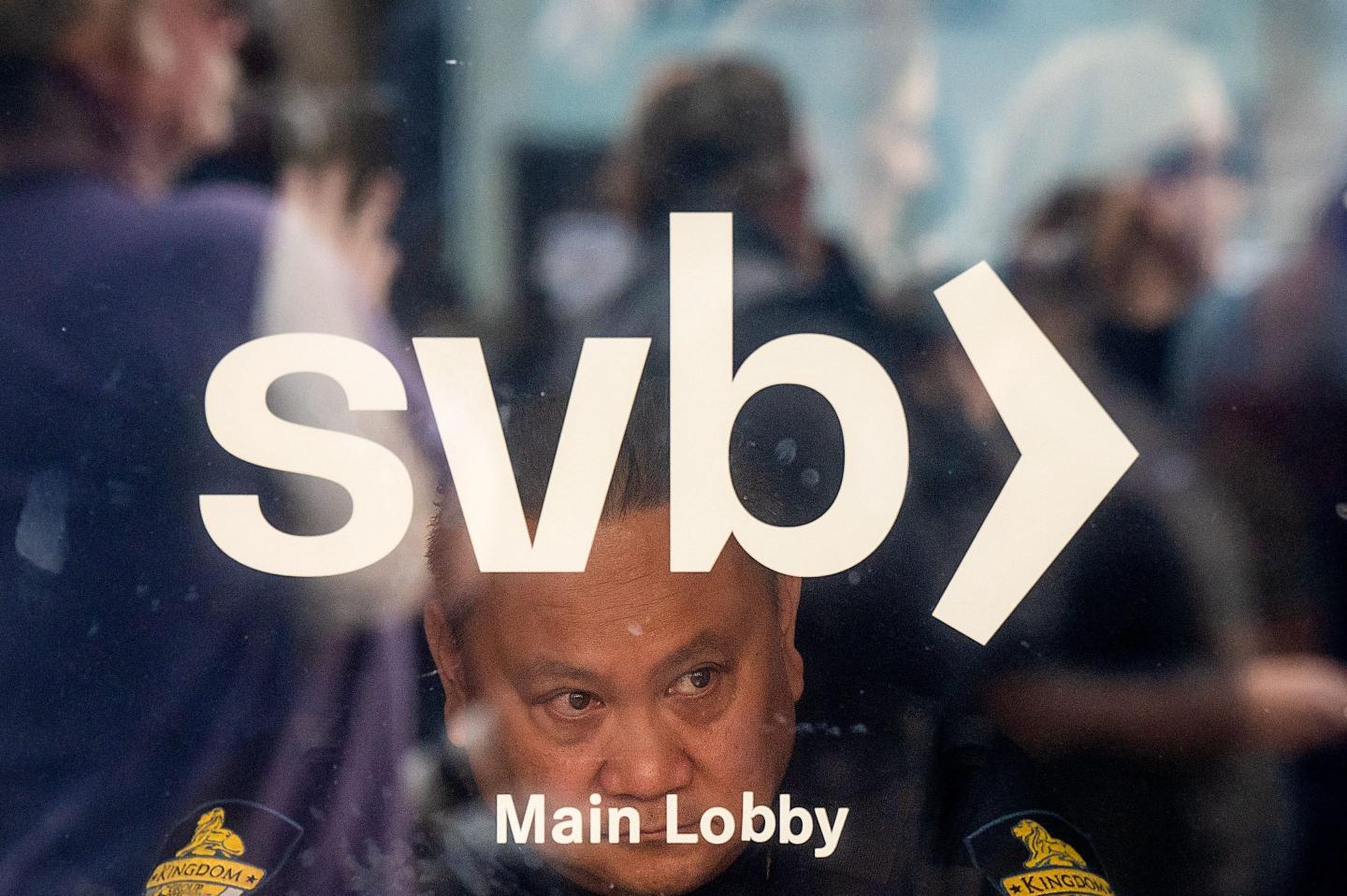 A security guard looks out a door as customers line up at Silicon Valley Bank headquarters in Santa Clara, California on March 13, 2023. - US President Biden sought to reassure Americans over the country's banking system on Monday, while insisting emergency measures would not be paid for by taxpayers, as additional banks came under stress following the collapse of Silicon Valley Bank last week, the second largest bank failure in history, and New York regulators took control of Signature Bank on Sunday.