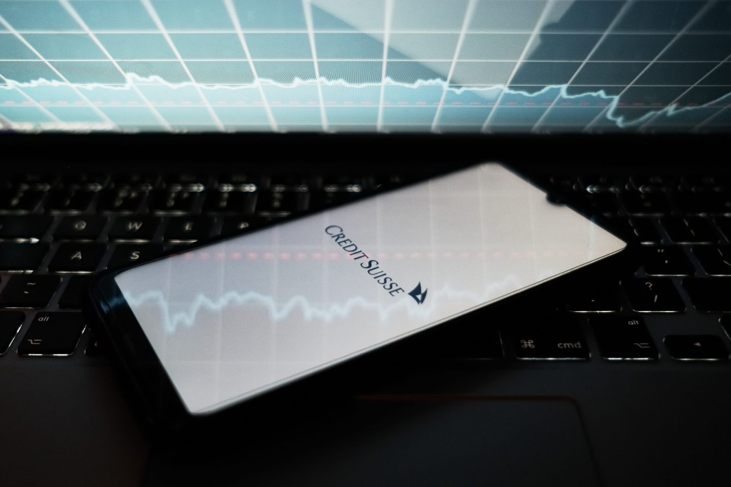 A Credit Suisse logo seen displayed on a smartphone screen and an illustrative stock chart background