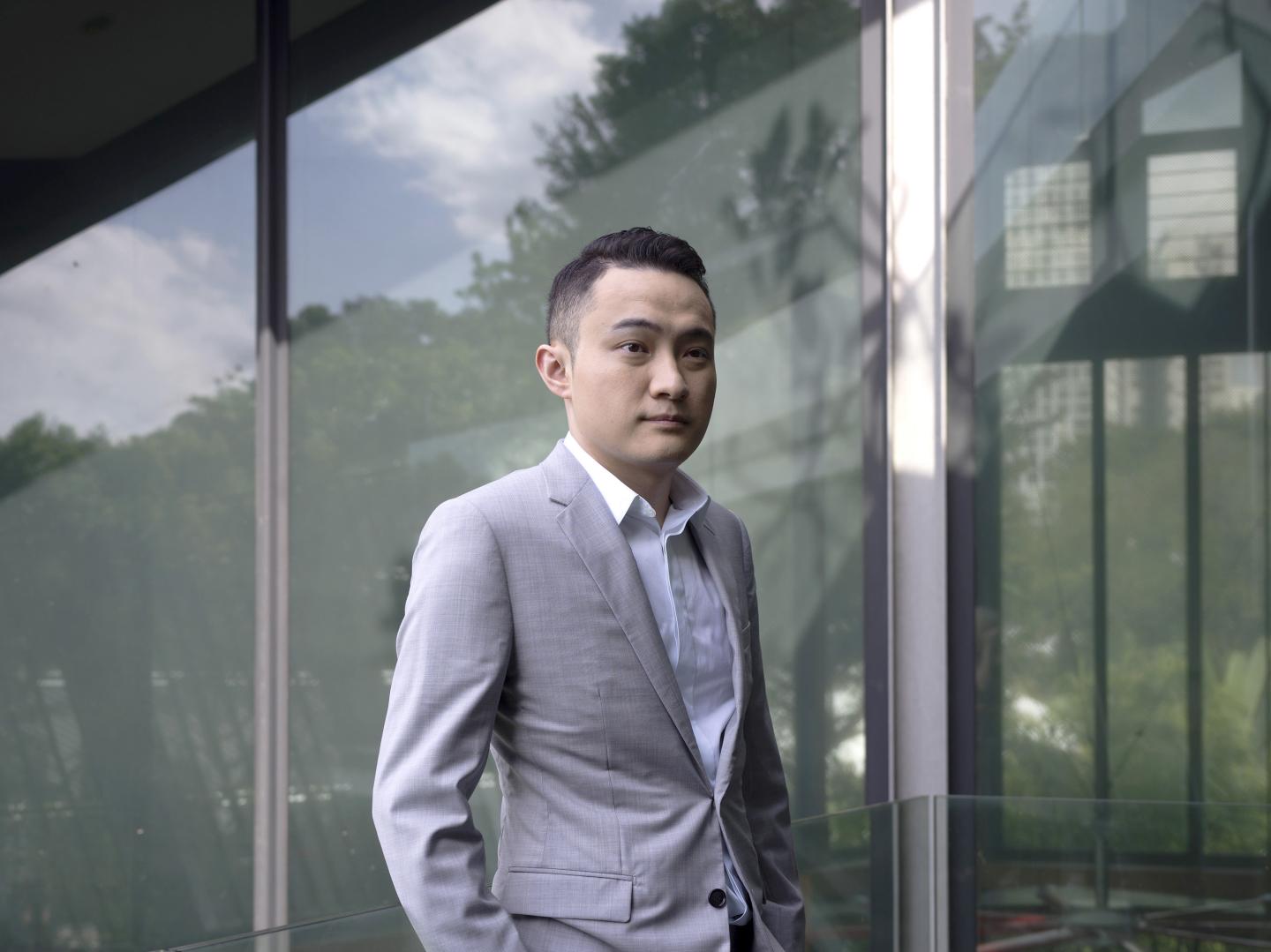 Justin Sun stands in front of a window wearing a gray suit.