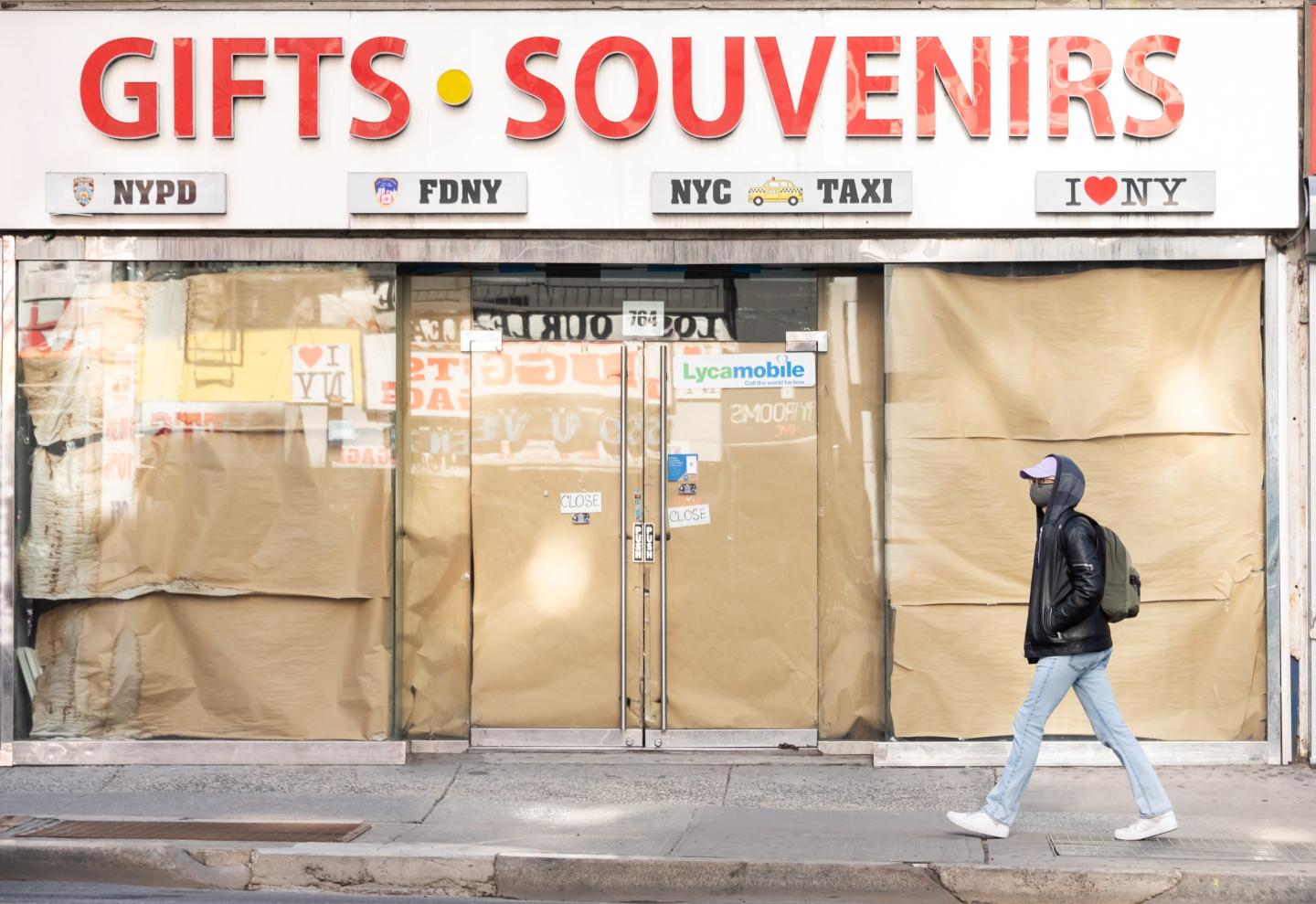Man walking in front of a boarded-up storefront in New York City
