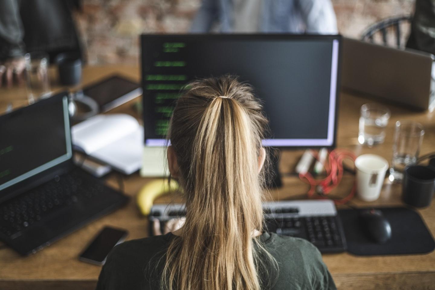 A woman sits at a screen looking at coding