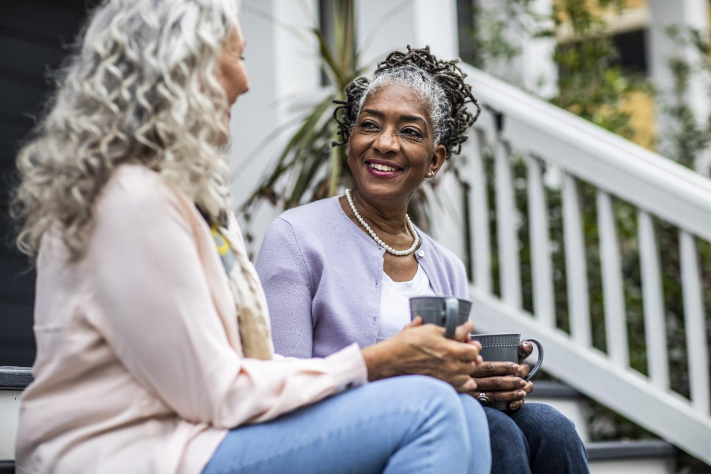 Two senior women drink coffee in front of a suburban home