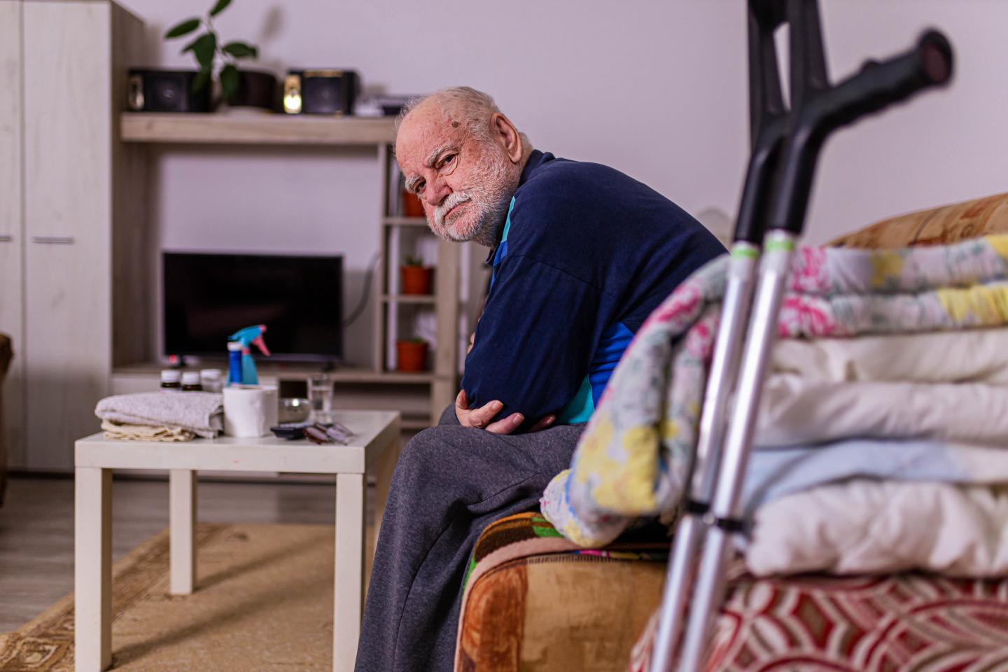 Photo of a man sitting on a couch next to a pair of cruntches