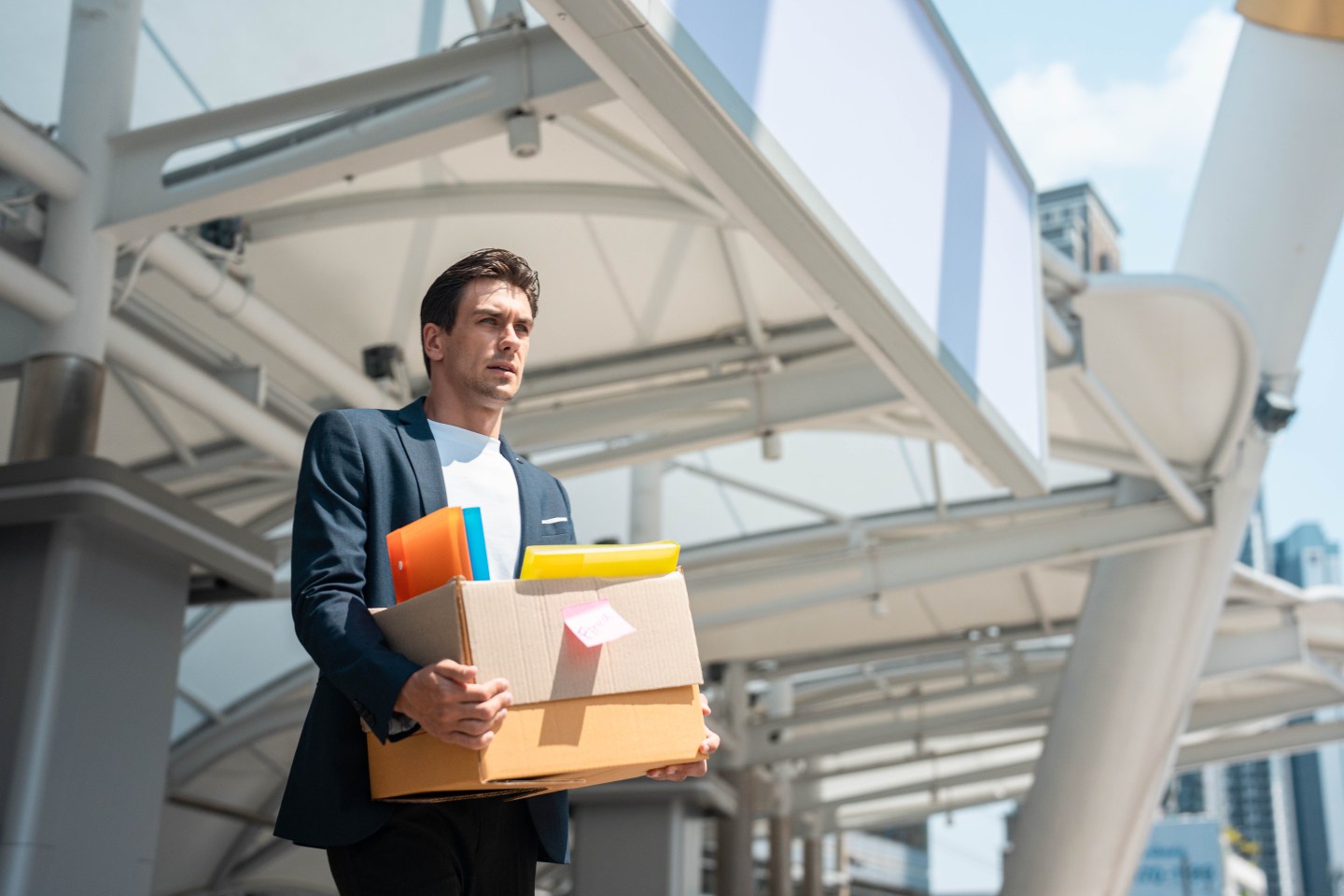 A laid off employee walking out of an office with a box of his belongings.