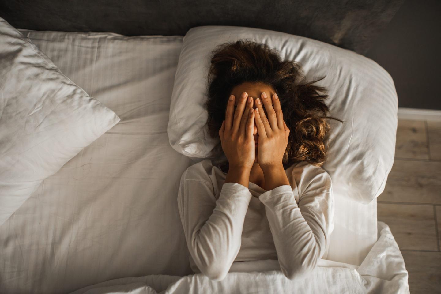 An upset-looking woman lies in her bed.