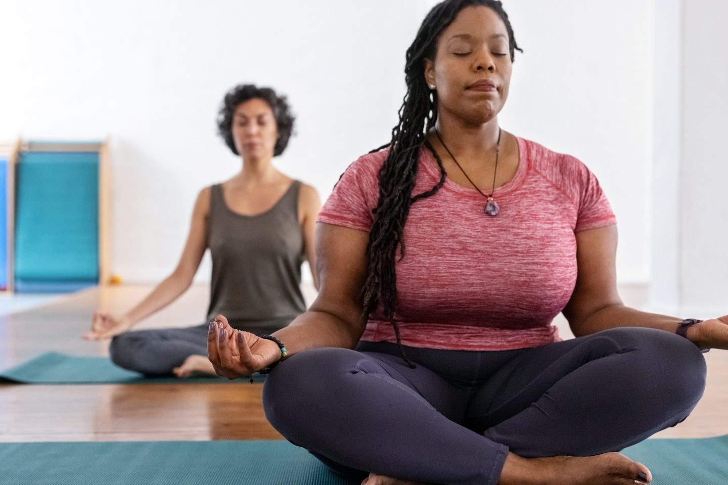 Healthy African woman meditating in yoga class with friends in background.