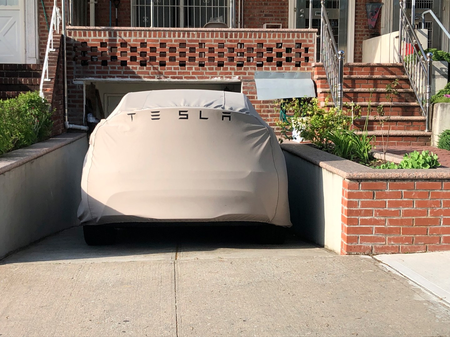 Covered Tesla electric car parked in a driveway in Queens, New York.