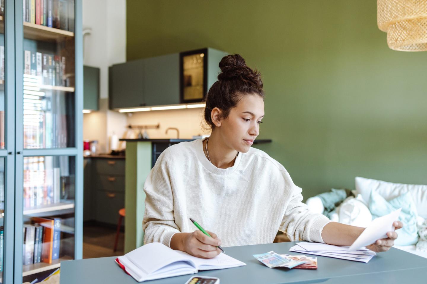 A woman sits at a desk with a calculator and notebook
