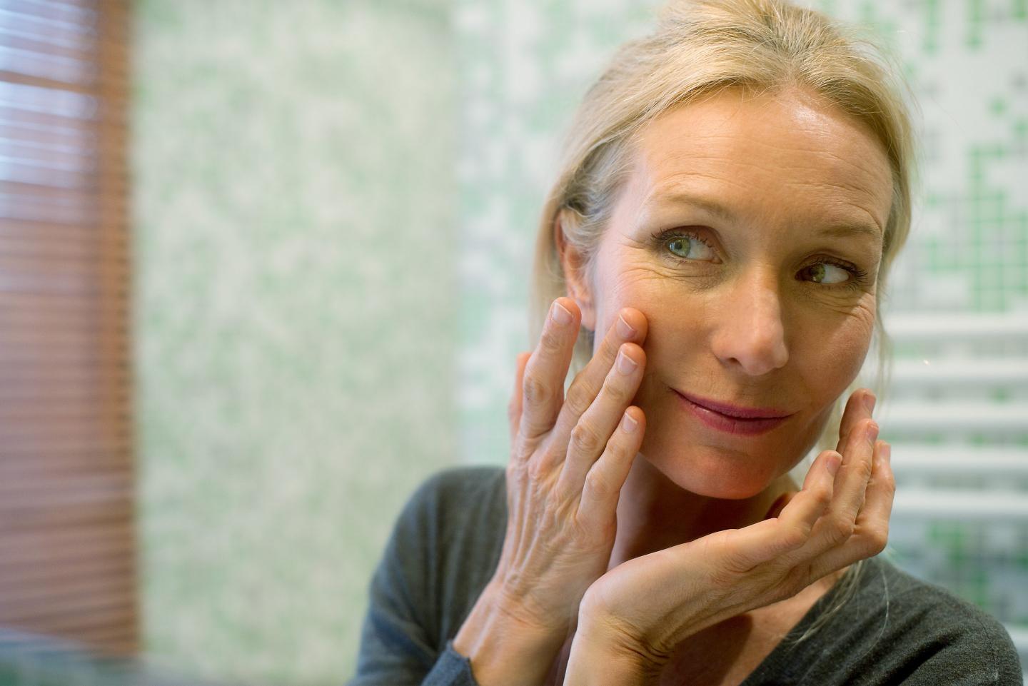 Woman looking at reflection in mirror with hand on cheek
