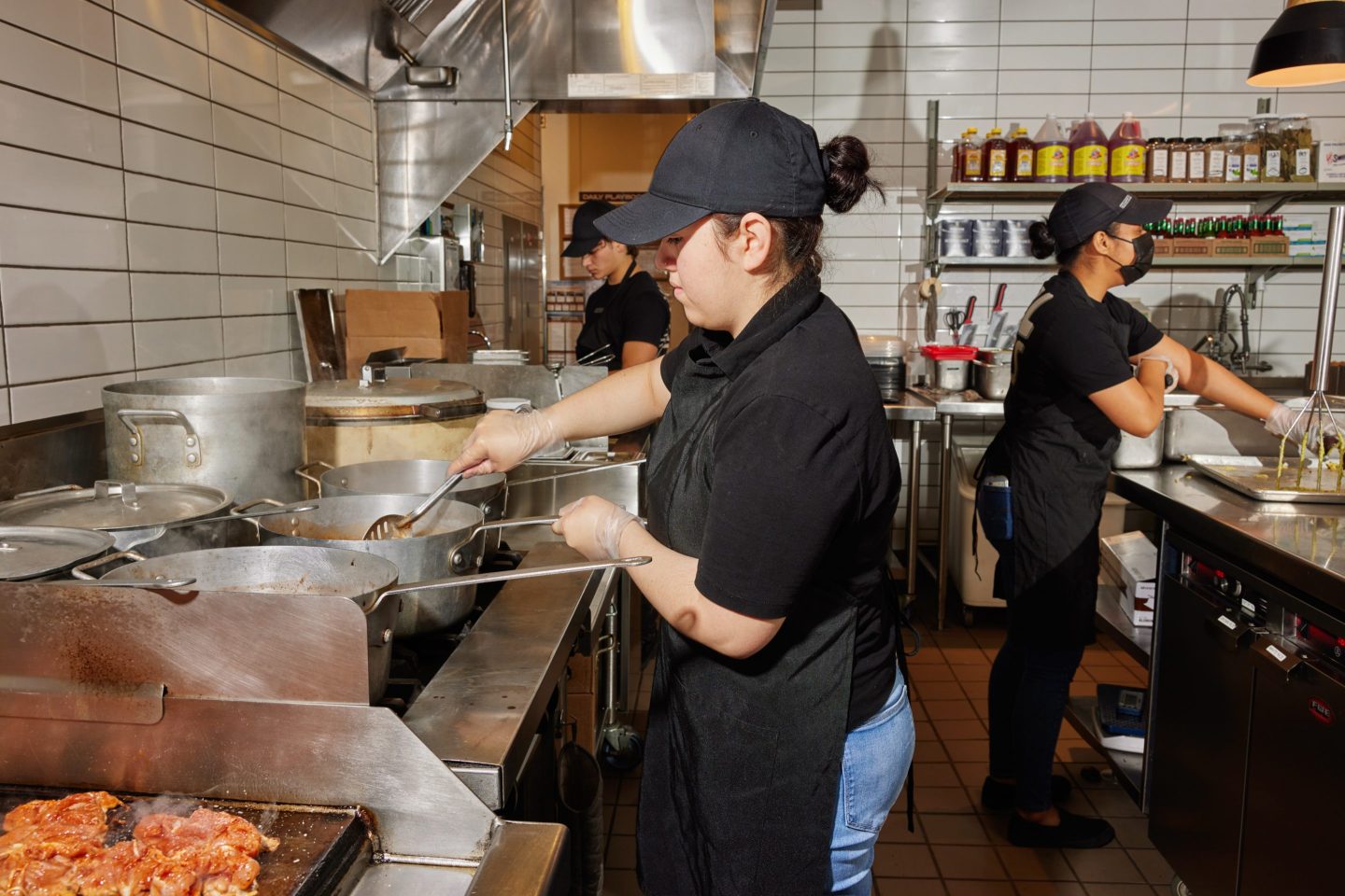 A Chipotle worker stirs beans cooking on the stove on the left while another peels avocados for guacamole on the right, at the Chipotle restaurant in Corona Del Mar, Calif.