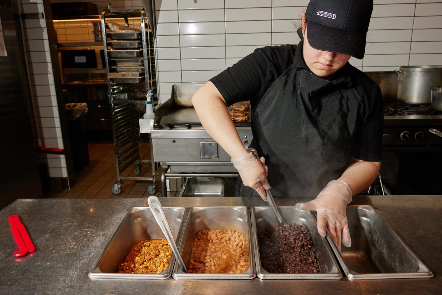 A Chipotle worker adds beans to the serving dishes during morning prep at the Chipotle restaurant in Corona Del Mar, Calif.