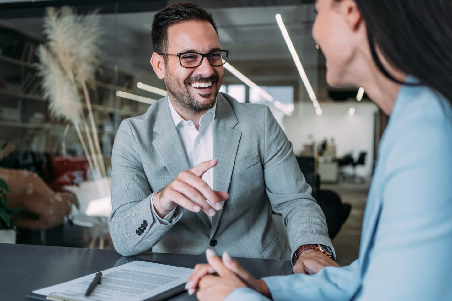A man in a business suit smiles as he talks to a woman in a boardroom