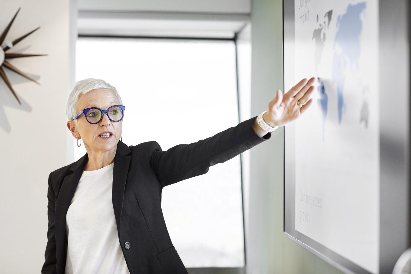 Senior businesswoman gesturing while looking at world map on screen