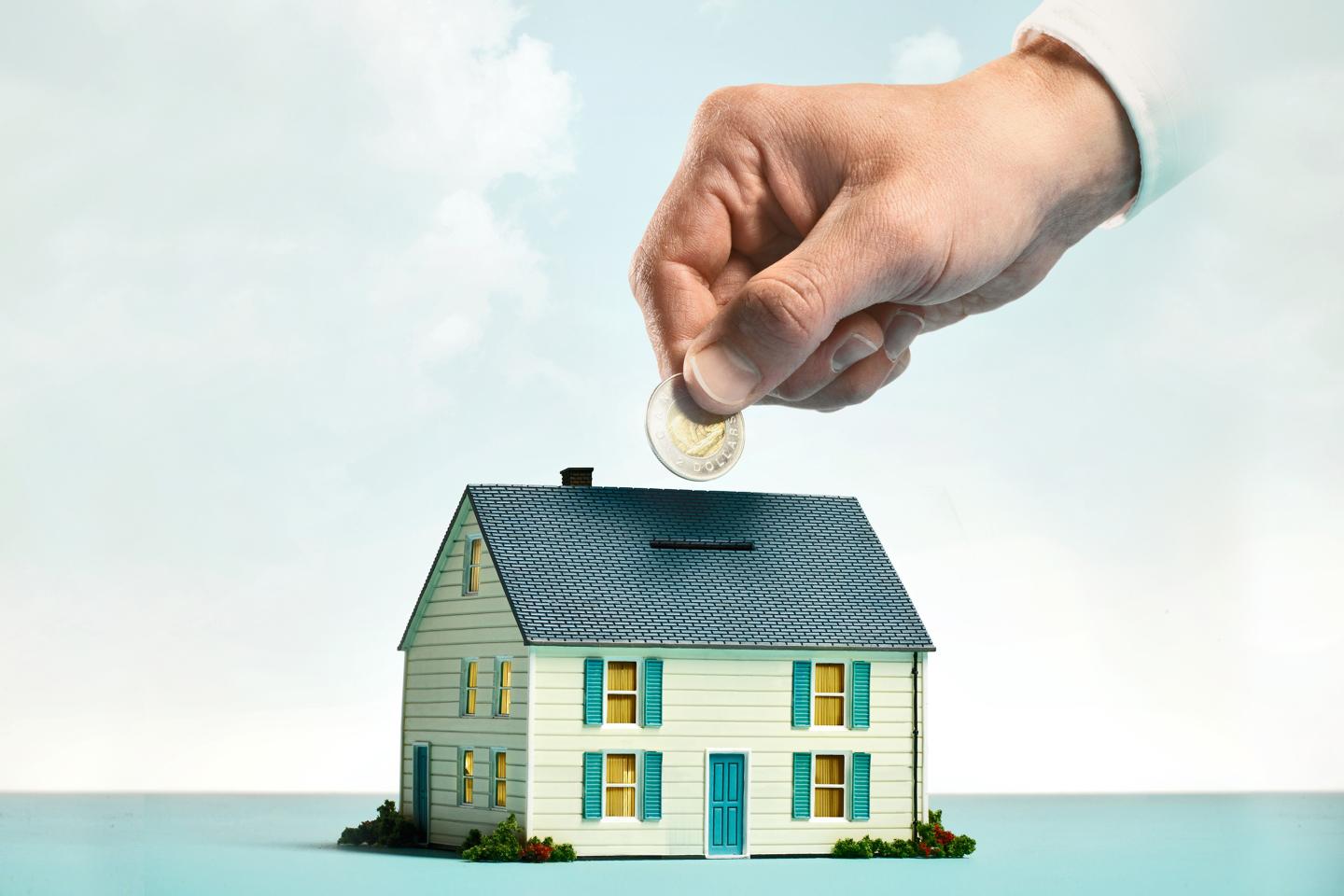 Photo illustration of a hand putting coins into a piggy bank shaped like a house