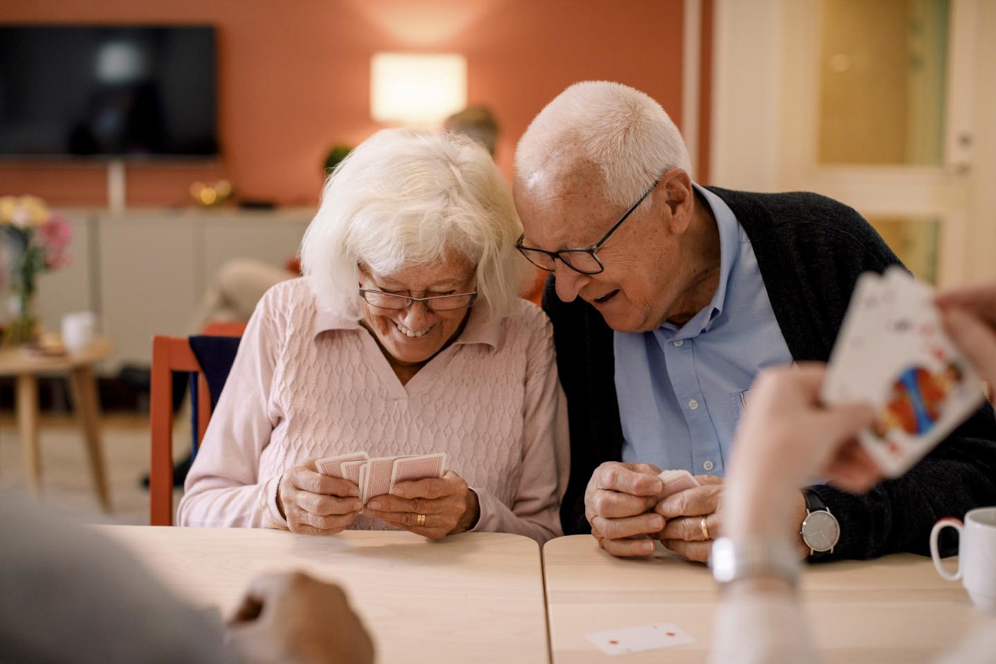 Senior man looking at elderly woman's cards while playing at nursing home.