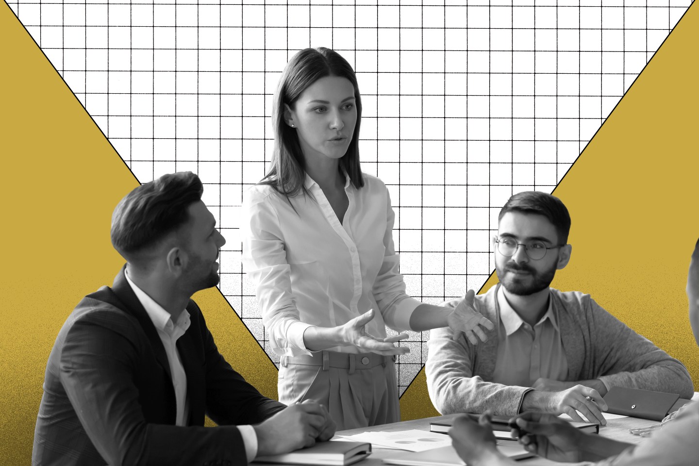 Photo of a few business associates having a conversation around a desk, three people are seated and one woman is standing and speaking.