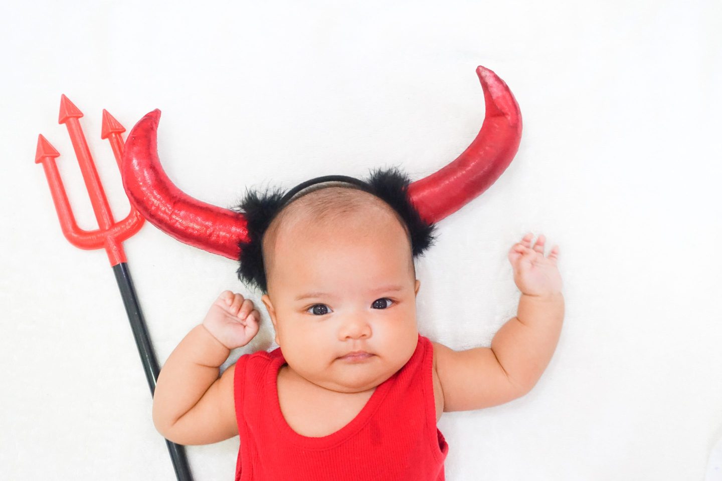 Photo of an infant dressed in a devil costume with a ptichfork.