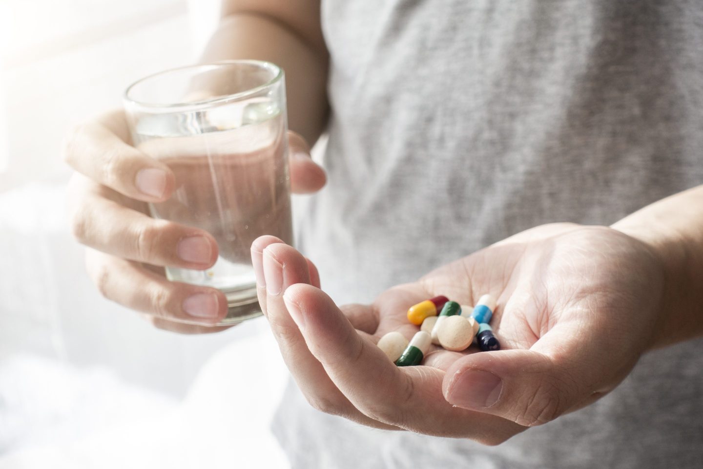 A person holding several multivitamins in one hand and a glass of water in the other