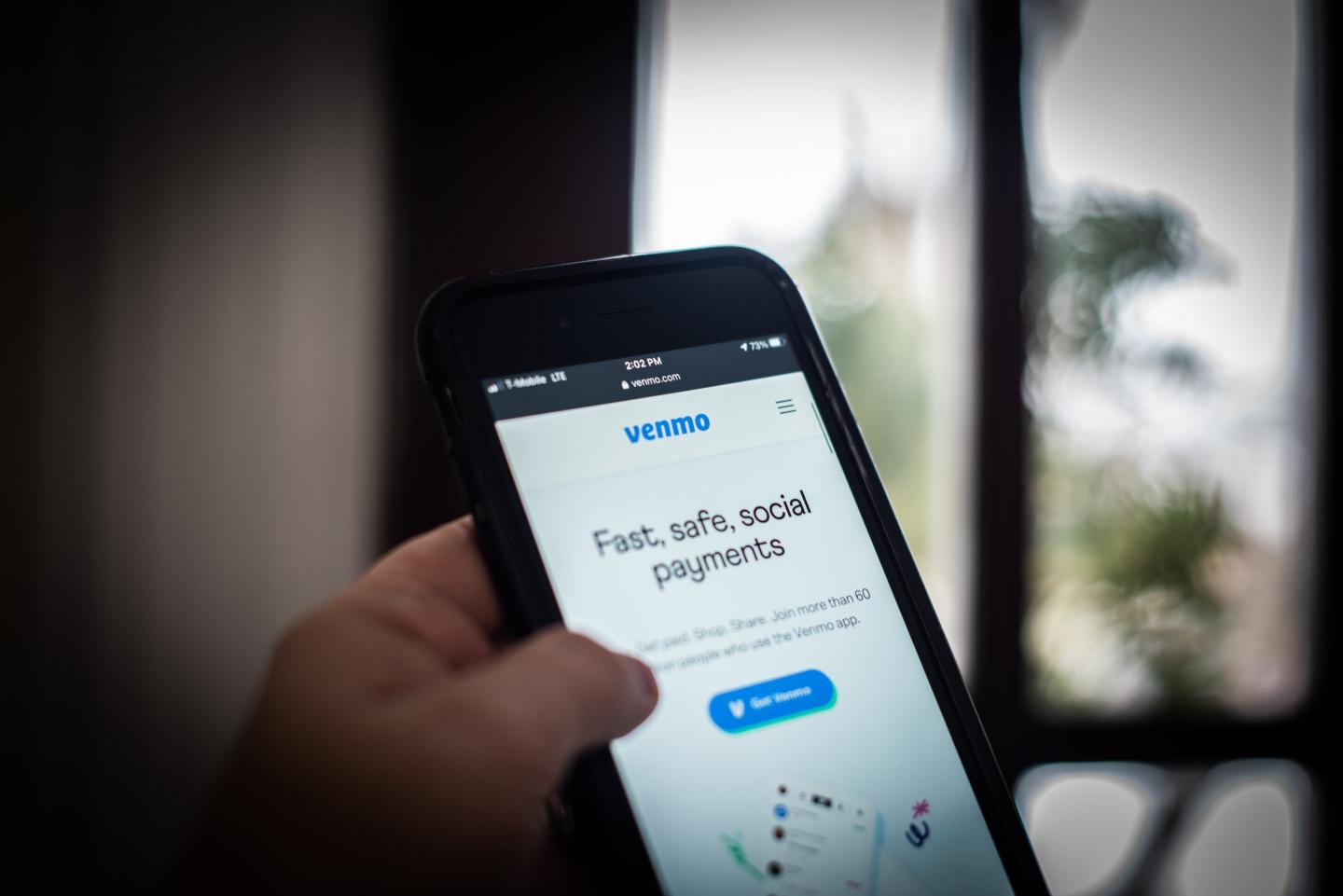 Someone holds a smartphone with the Venmo app open in front of a window.