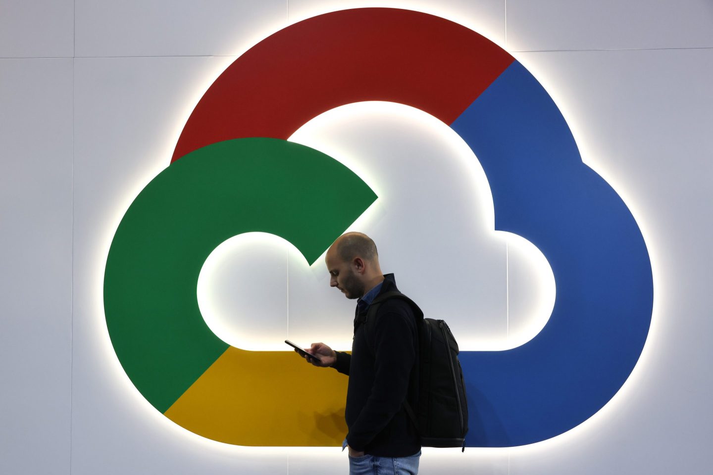 A man looks at a smartphone in front of a Google Cloud logo.