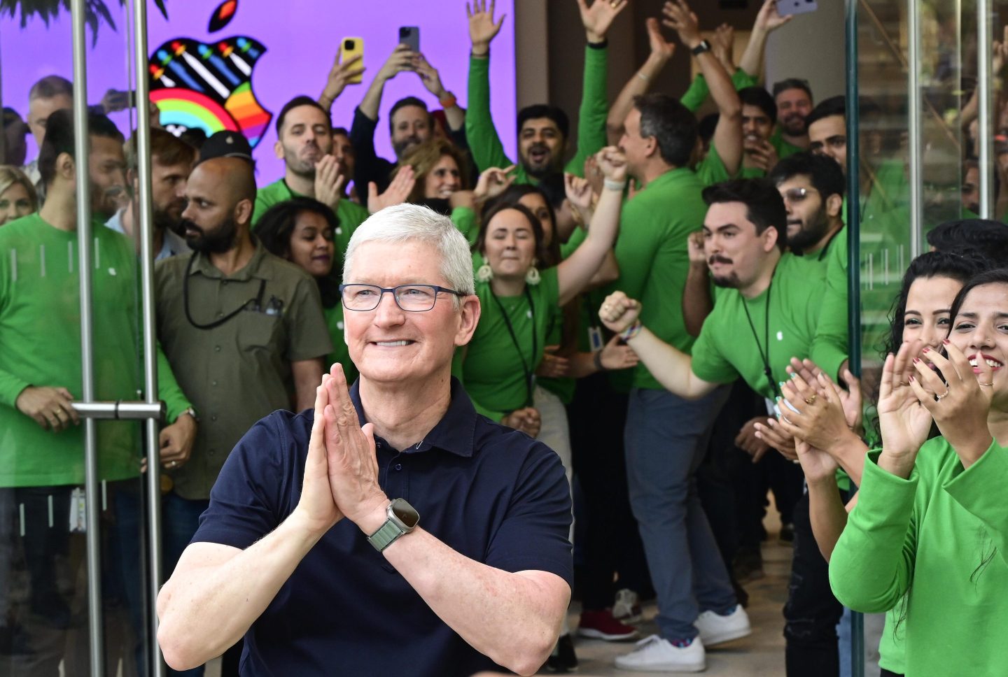 A picture of Tim Cook joining his palms with a crowd of people cheering at the back.