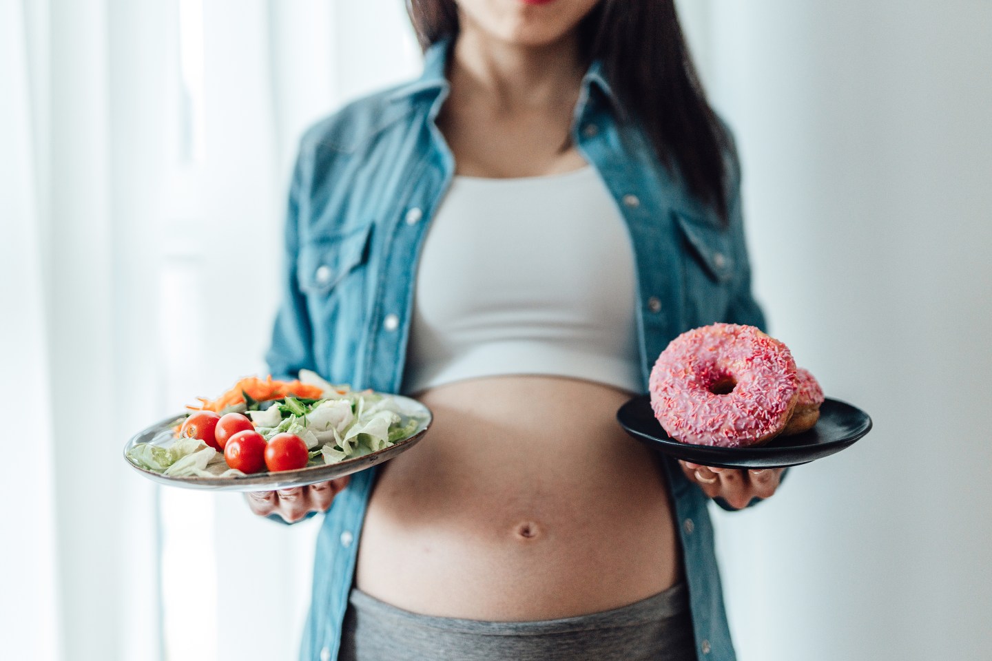 Photo of a pregnant woman choosing between vegetables and doughnuts