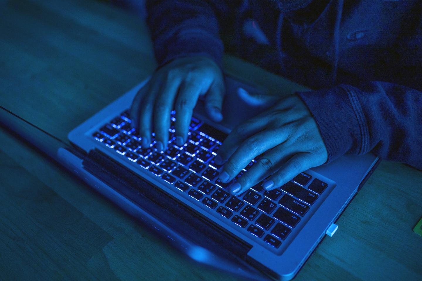 An unseen person types on a laptop