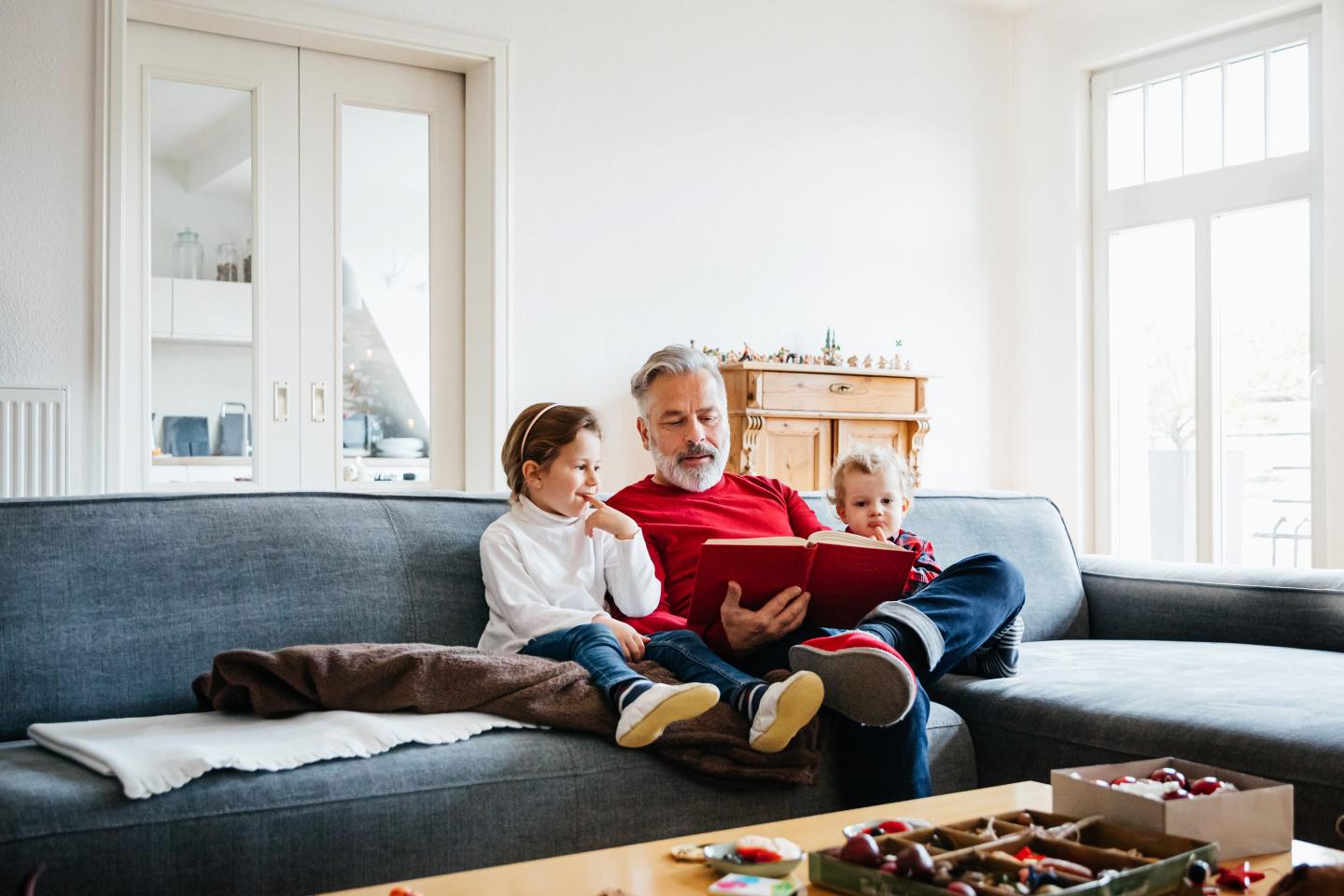 Two Young Grandchildren Sitting With Grandpa Reading Book