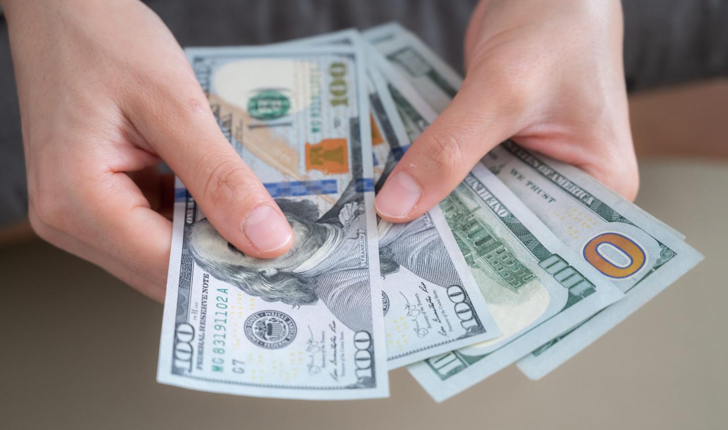 Close-up photo of someone holding and counting American dollar banknotes in her hand.