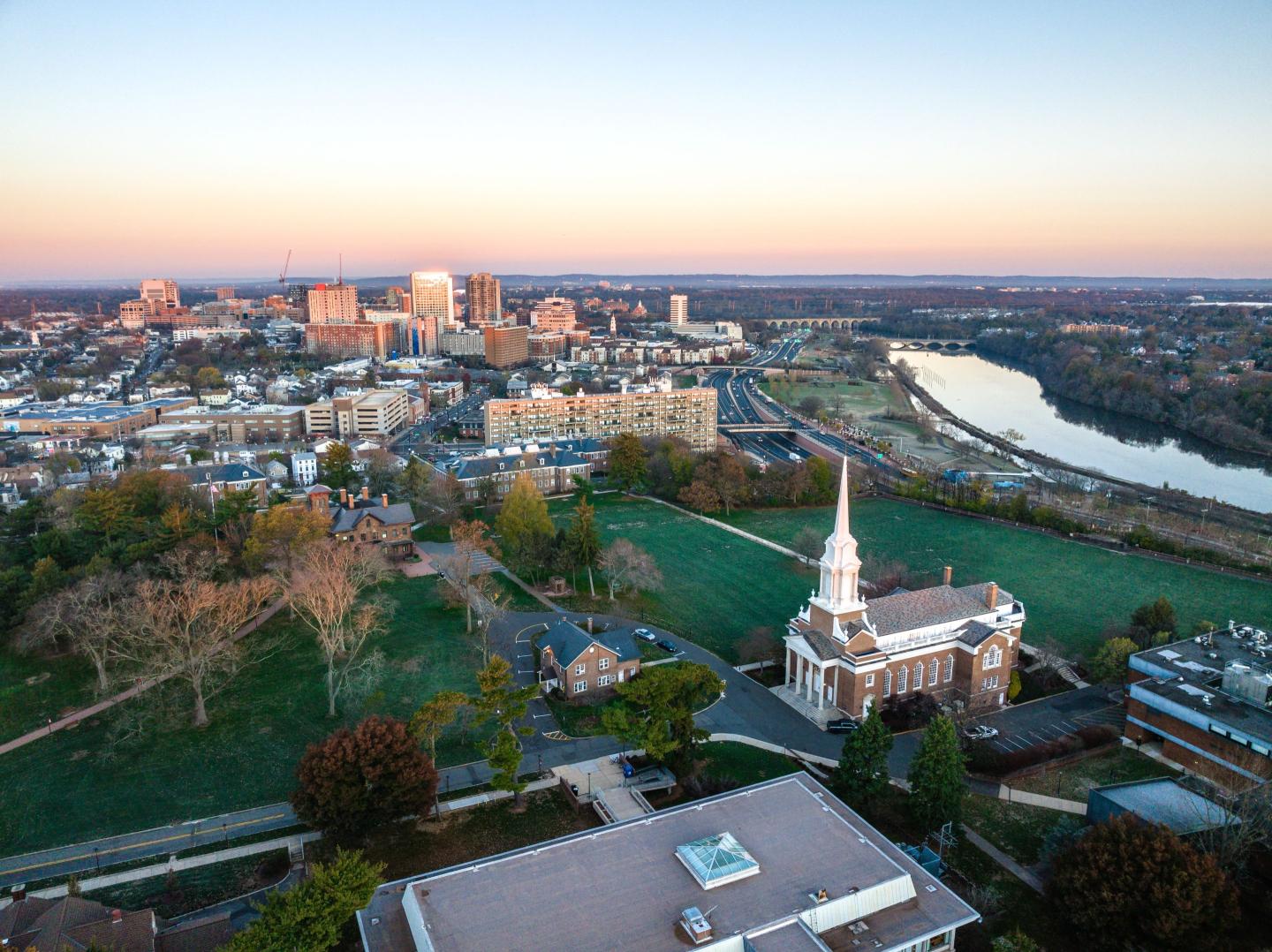 A drone view of a city skyline with buildings near the river at sunrise in New Brunswick, Rutgers, Hub City, USA
