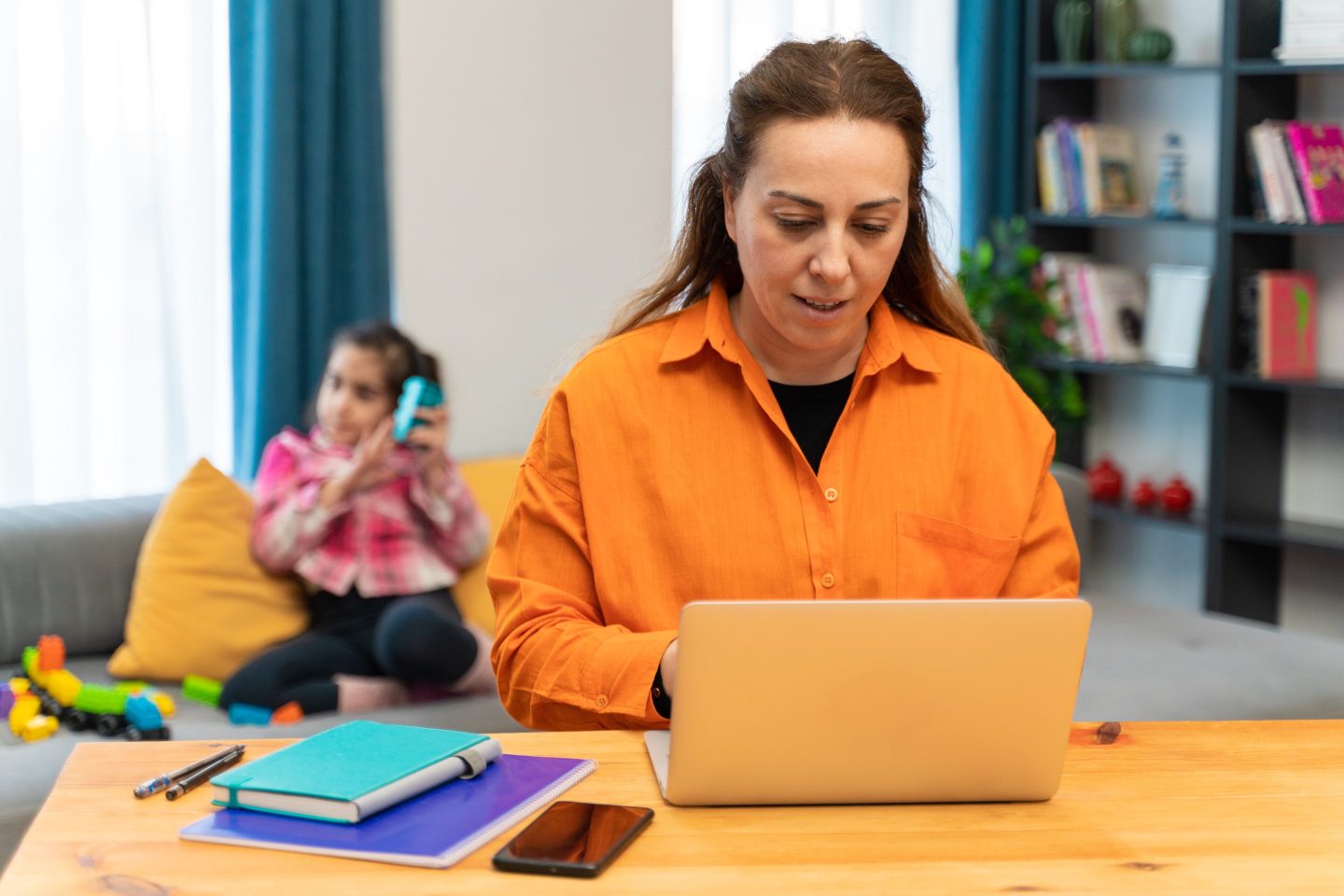 Young daughter plays beside her working mother in a home office