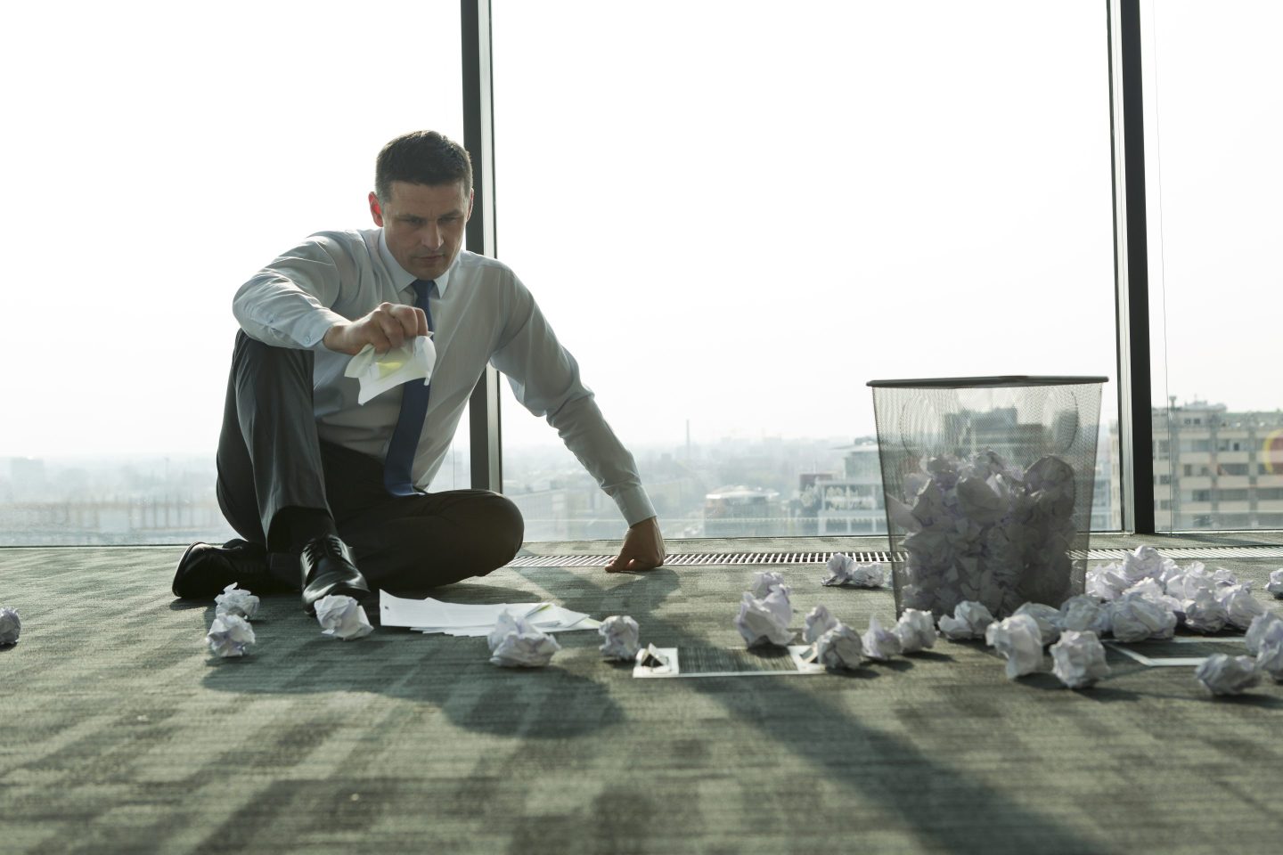 Businessman sitting on office floor surrounded by crumpled paper