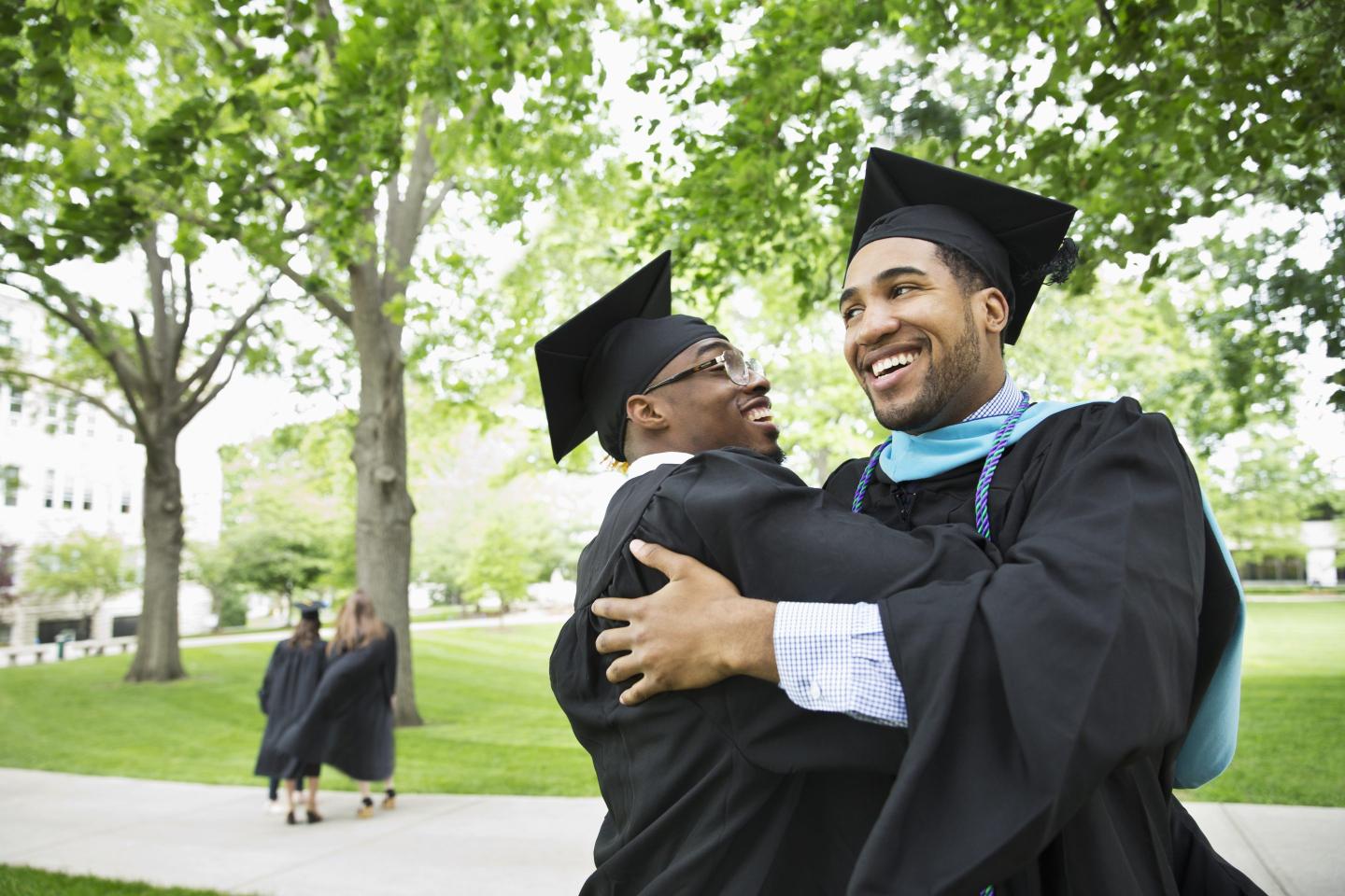 Two Black male graduates hug in their graduation caps and gowns.