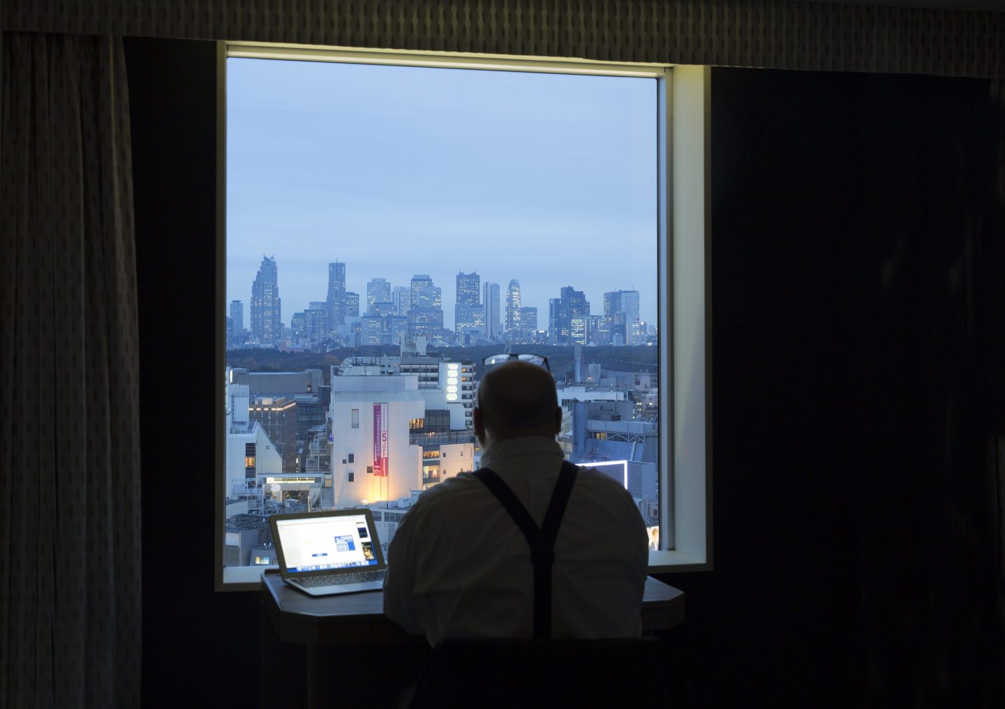 Man looking out of hotel window at Shinjuku business district