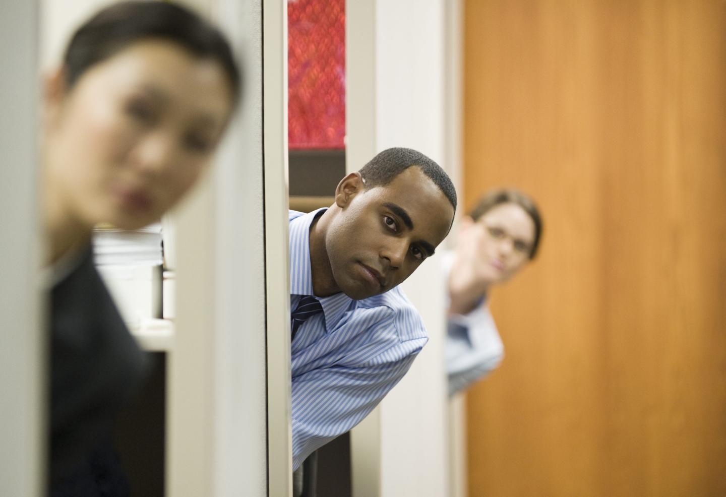 Three employees poke their heads out from their cubicles.
