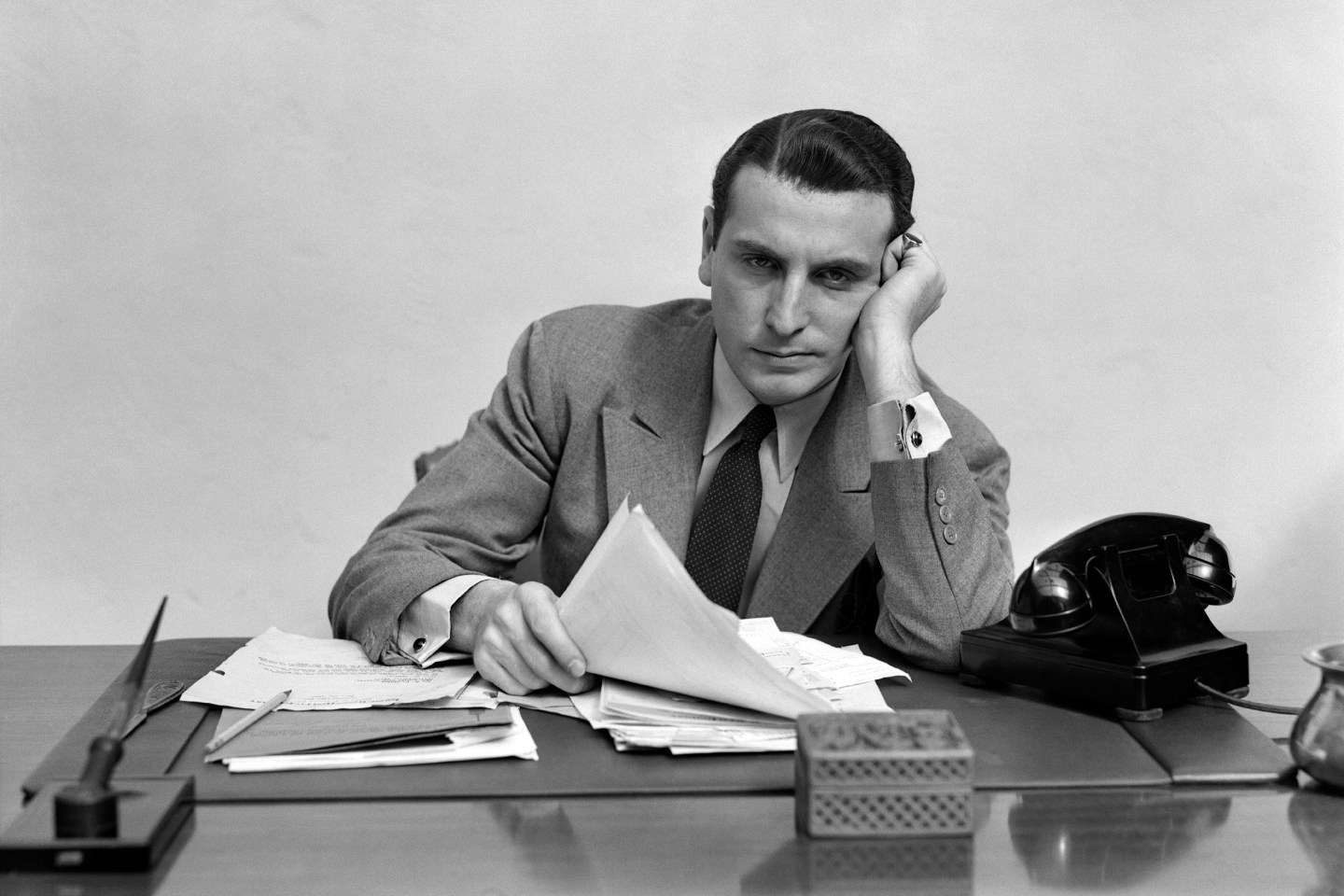 Tired, overworked businessman leaning on elbow over desk looking sad.