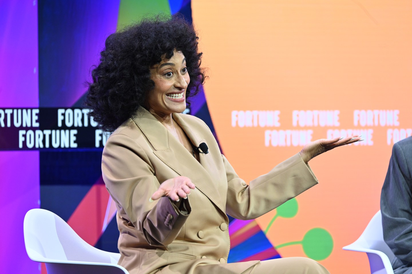 Tracee Ellis Ross sits with her hands out and palms up in front of a Fortune-branded backdrop, smiling.