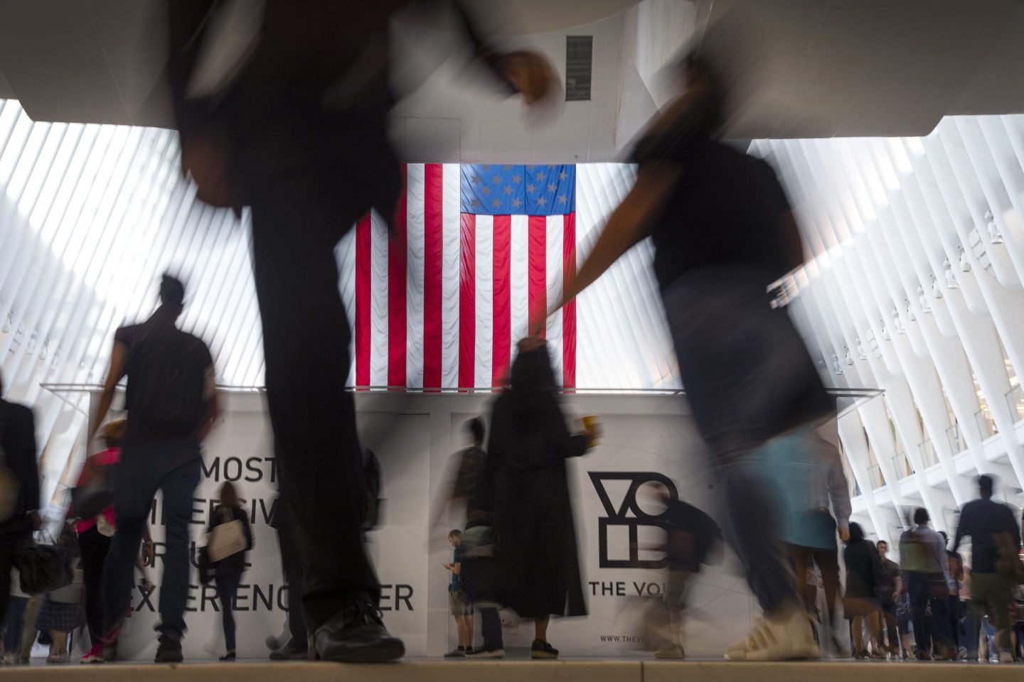 People walk past an American flag inside the Oculus, part of the World Trade Center transportation hub, at the start of a work day in New York, Sept. 11, 2019.