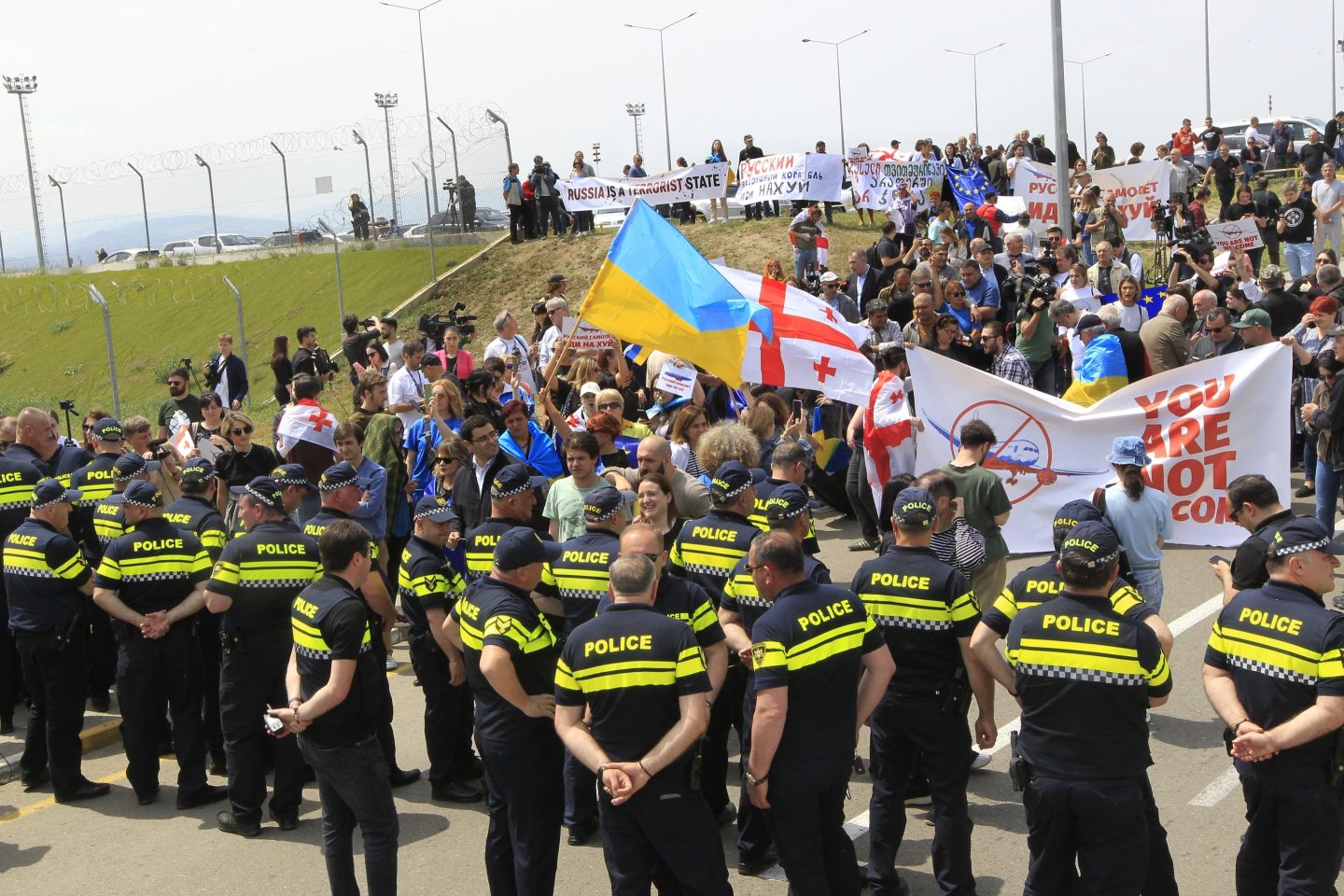 Georgian opposition activists with Georgian and Ukrainian national flags attend a protest against the resumption of air links with Russia standing behind a police line at the International Airport outside Tbilisi, Georgia on May 19, 2023.