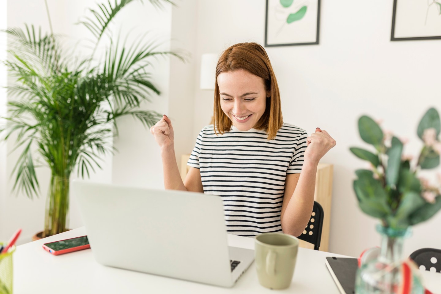 Cheerful young woman celebrating her achievement while reading good news on laptop from home office
