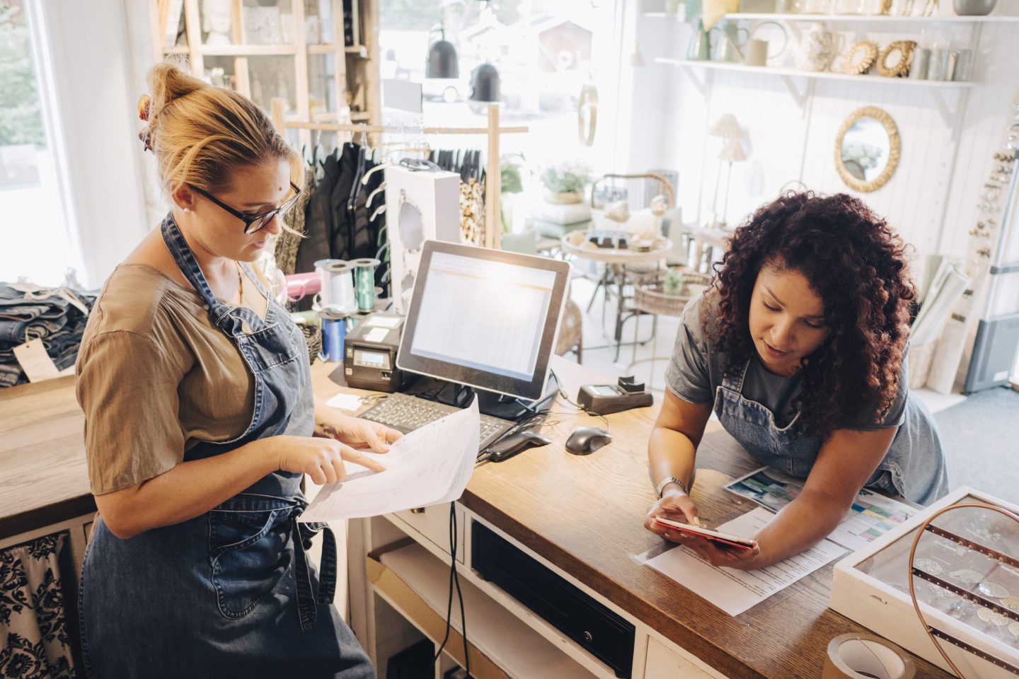 Colleagues in a small shop discussing receipts while working on a tablet