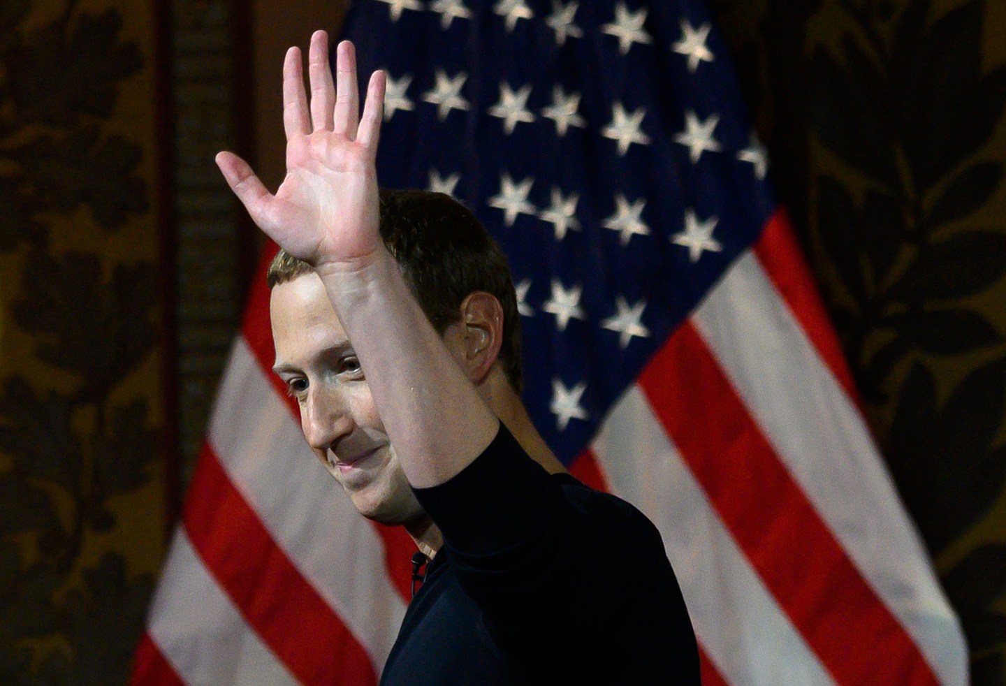 Facebook founder Mark Zuckerberg waves in front of US flag.
