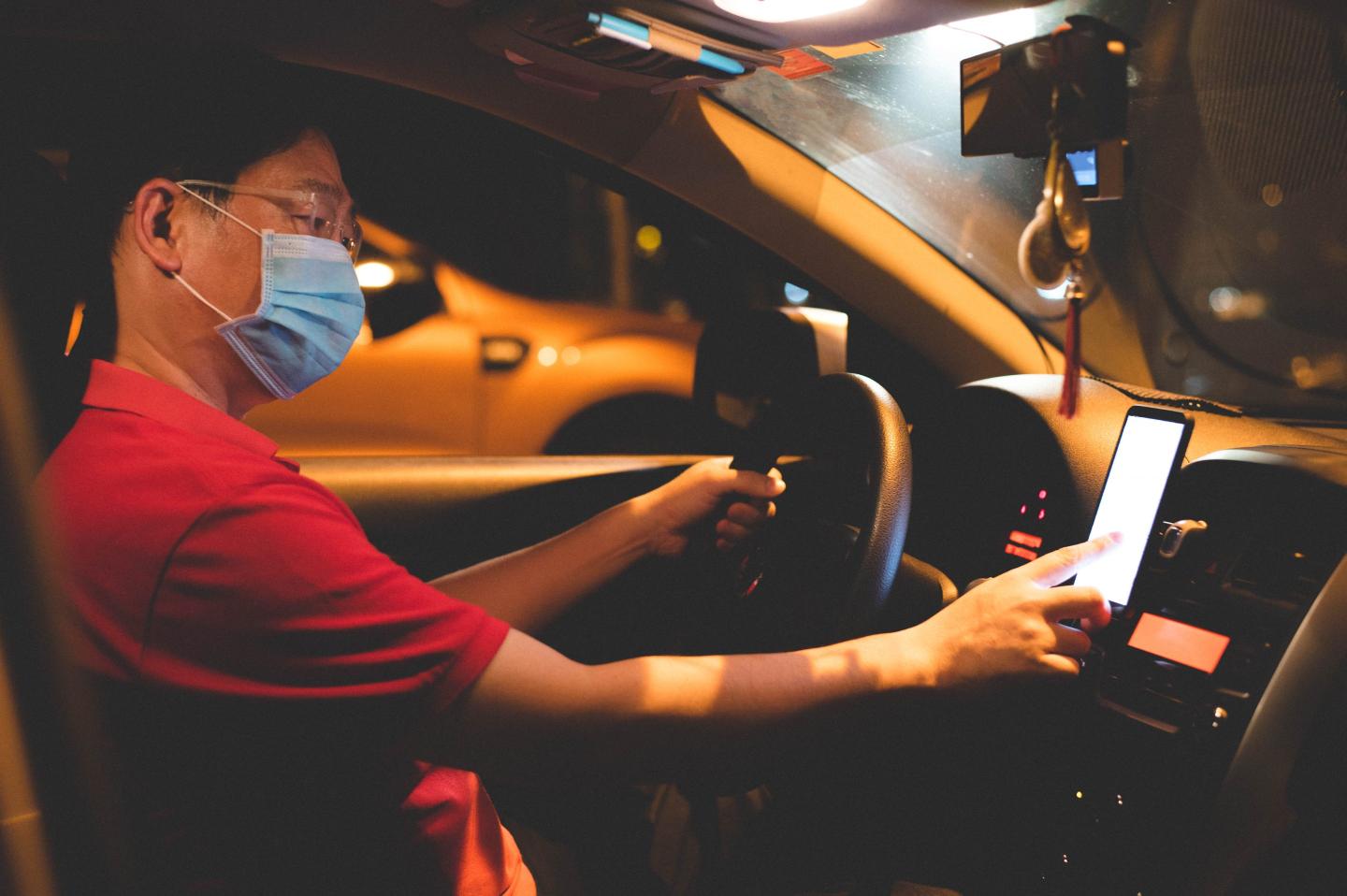 An Uber driver checks his phone while sitting in the drivers seat of his car.