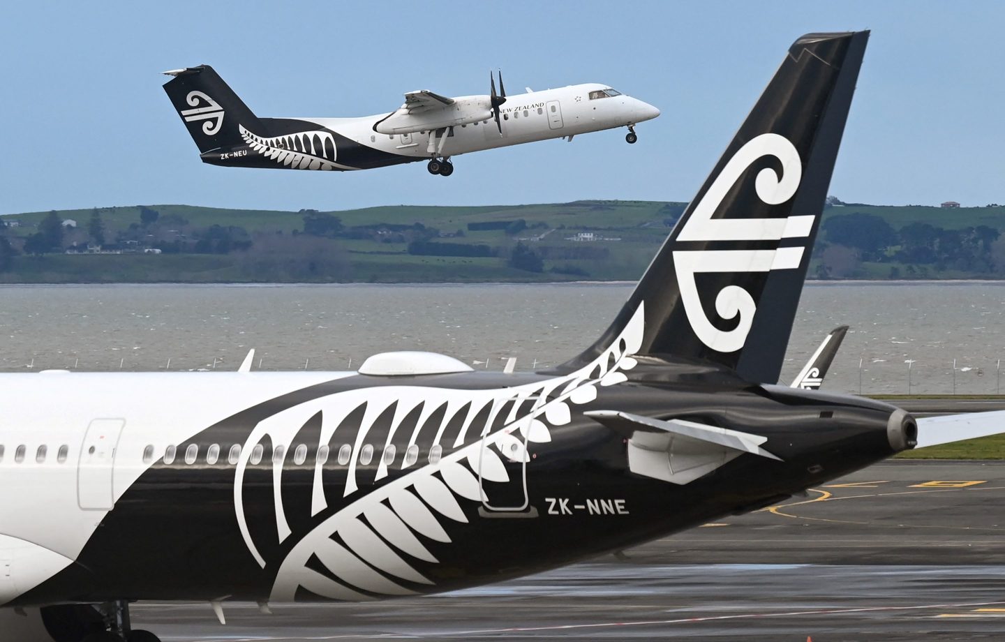 An Air New Zealand plane takes off from Auckland Airport while another is parked on the tarmac.